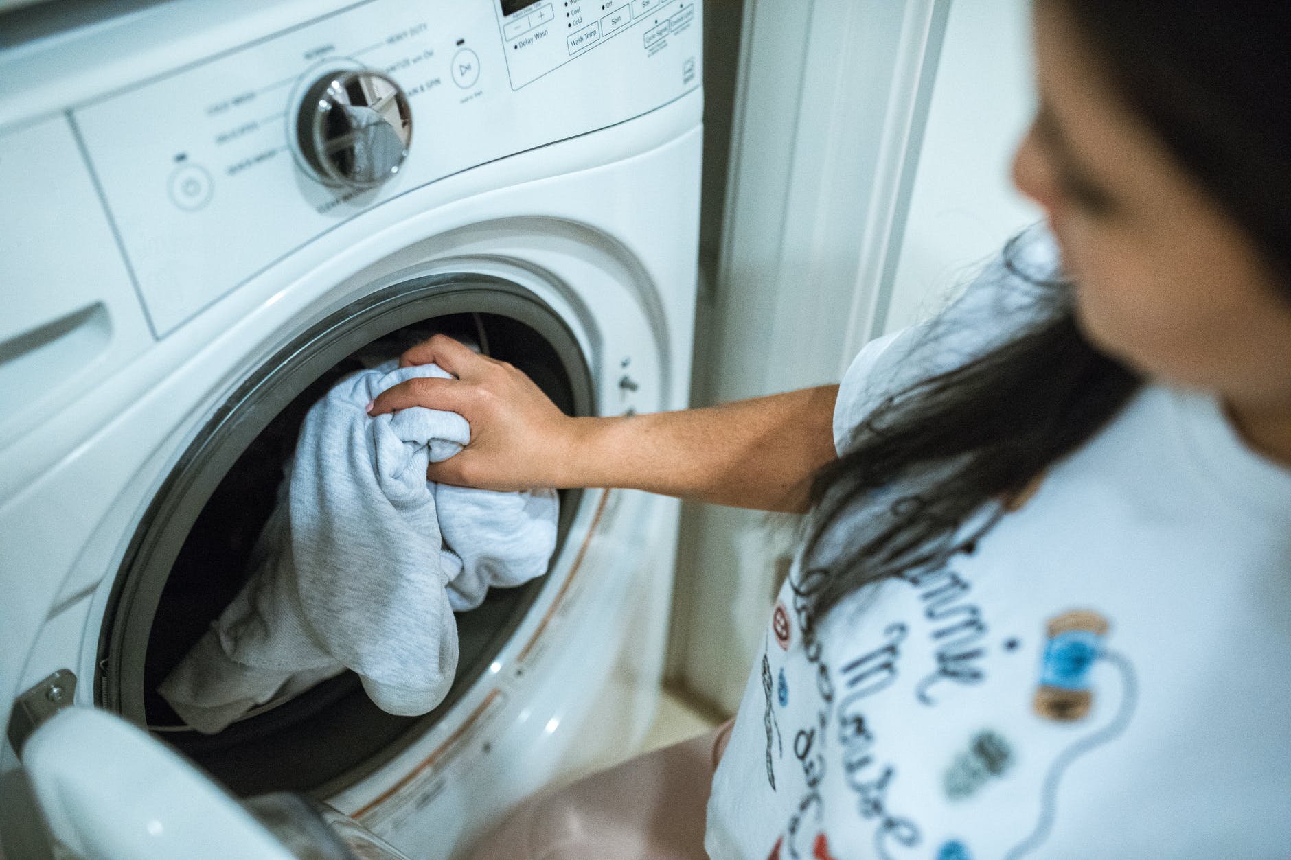woman in gray shirt standing in front of white front load washing machine